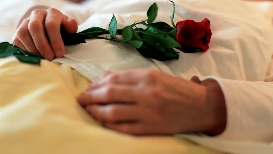 Hände einer Verstorbenen halten eine Rose.