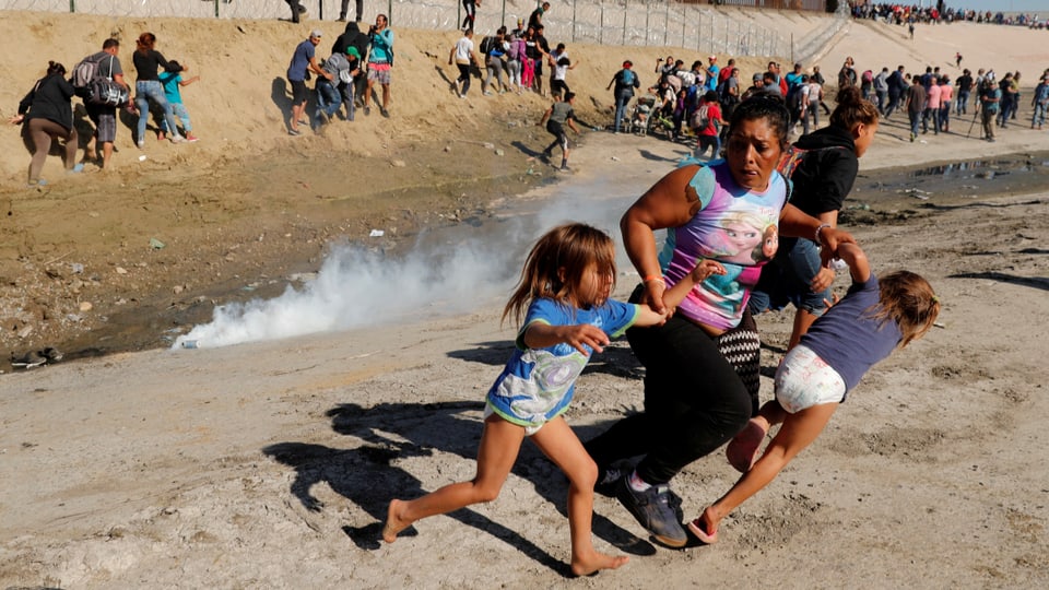 Eine Migrantin aus Honduras flüchtet mit ihren beiden Kindern vor der Tränengas-Wolke. 
