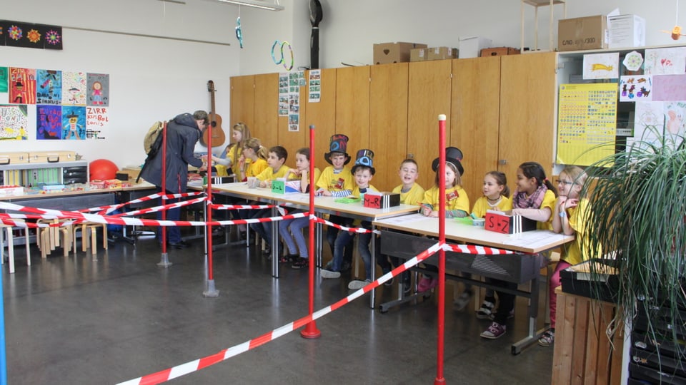 Schüler sitzen an einem langen Tisch. Absperrbänder davor.