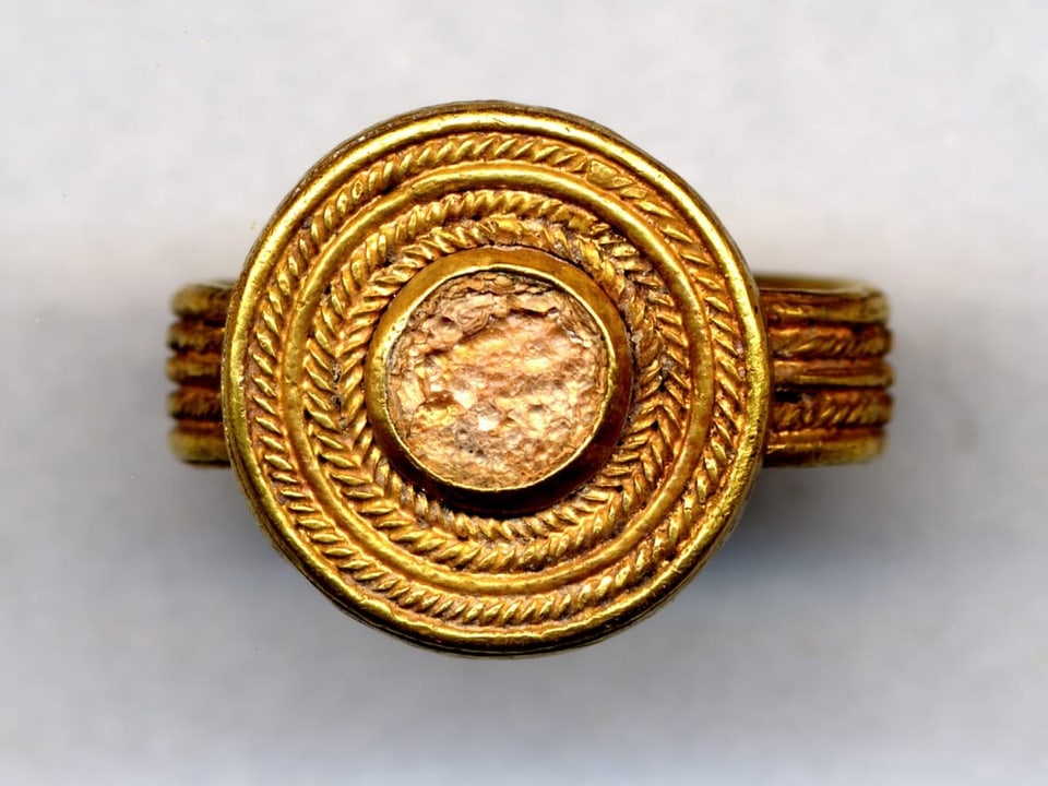 goldener Ring mit rundem Stein, darum herum goldene Kreise