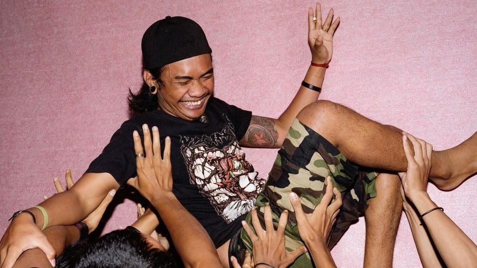 Eine Gruppe Menschen wirft einen lachenden Heavy-Metal-Sänger in die Luft.