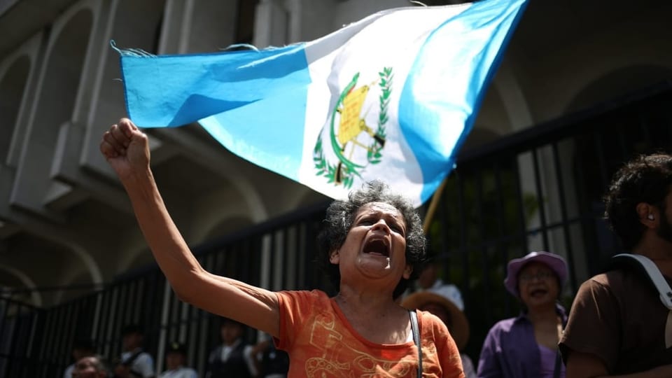Eine Frau protestiert, hinter ihr weht die Flagge von Guatemala.