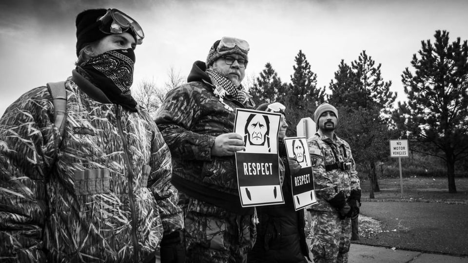 Protestierende halten ein Schild mit Personen der indigenen Bevölkerung hoch.