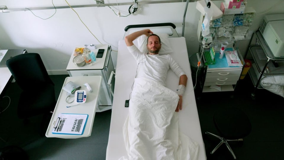 Ein Mann liegt zentral auf einem Bett in einem Klinikzimmer