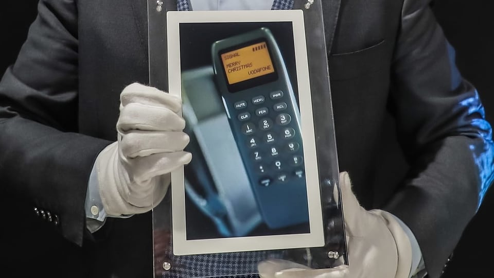 Eine Person hält einen Rahmen mit einem Bild eines Handys in der Hand.