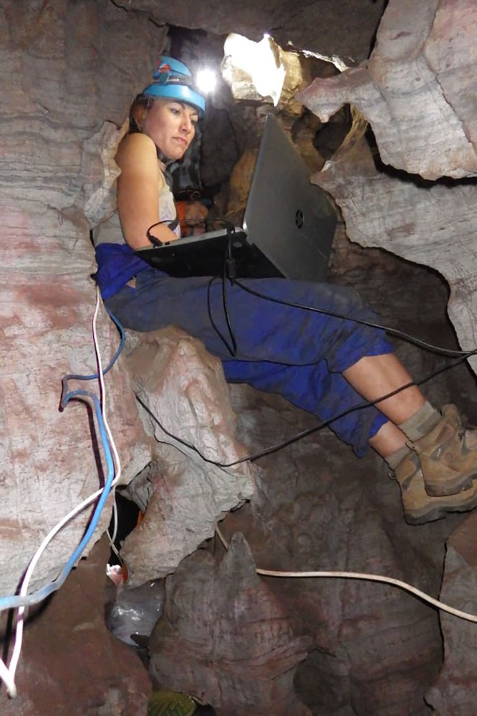 Eine Frau sitzt mit Laptop auf dem Schoss in einer Felsspalte.