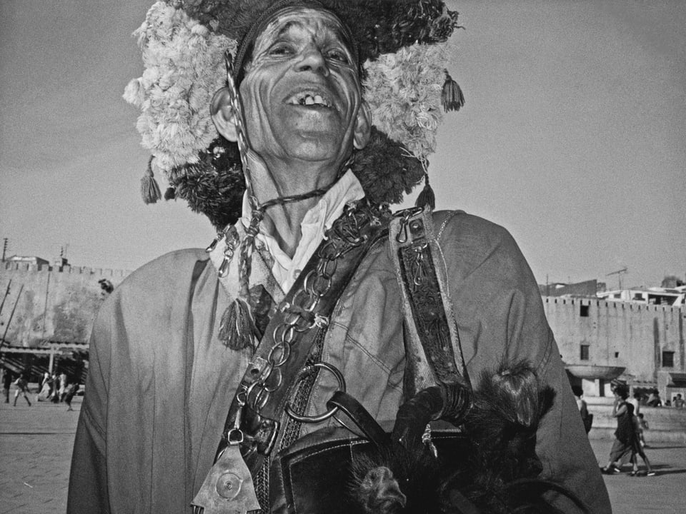 Schwarz-Weiss-Foto: Ein Mann mit einem breitkrempigen Hut aus Stoffquasten aus der Froschperspektive fotografiert. 