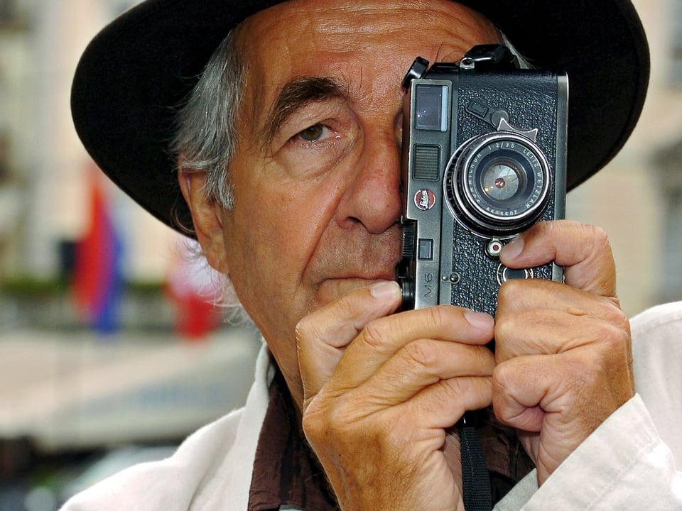 René Burri deckt sein halbes Gesicht mit einem Fotoapparat ab.