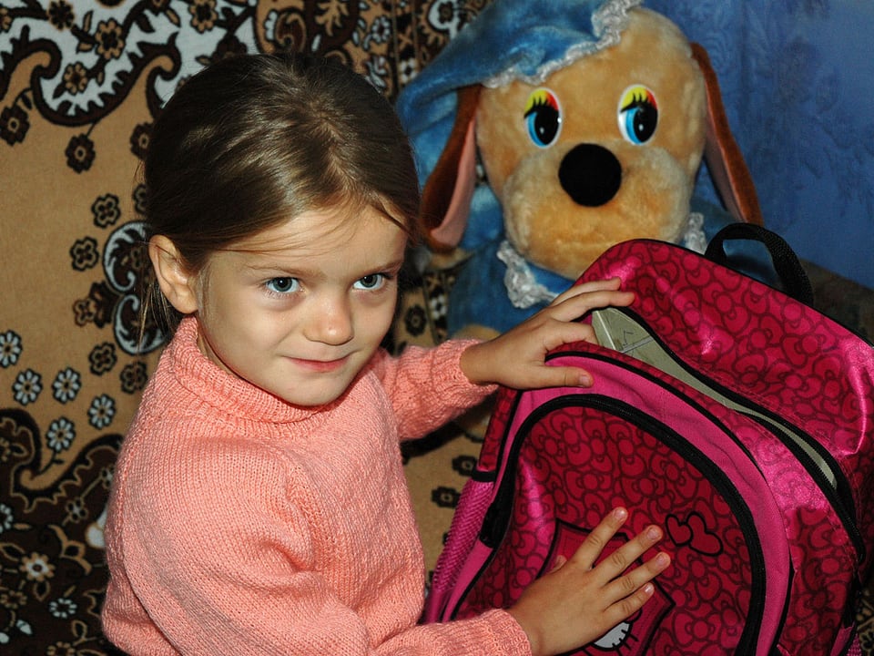 Ein kleines Mädchen zeigt stolz ihren rosaroten Rucksack.