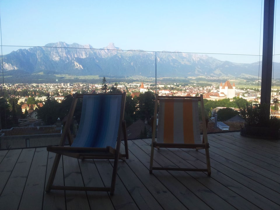 Balkon mit zwei Liegestühlen, im Hintergrund die Stadt Thun und die Berge.