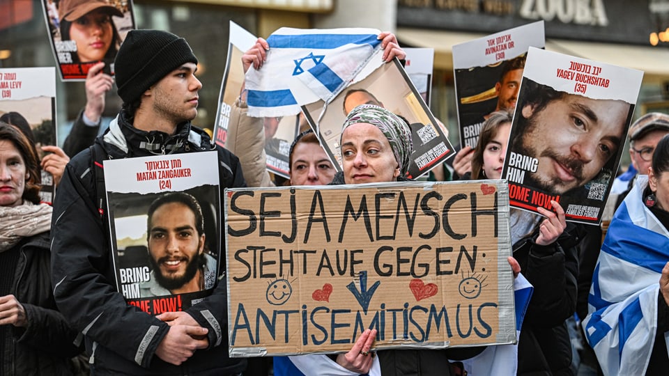 Mehrere Menschen stehen mit Plakaten und Israel-Flaggen zusammen.
