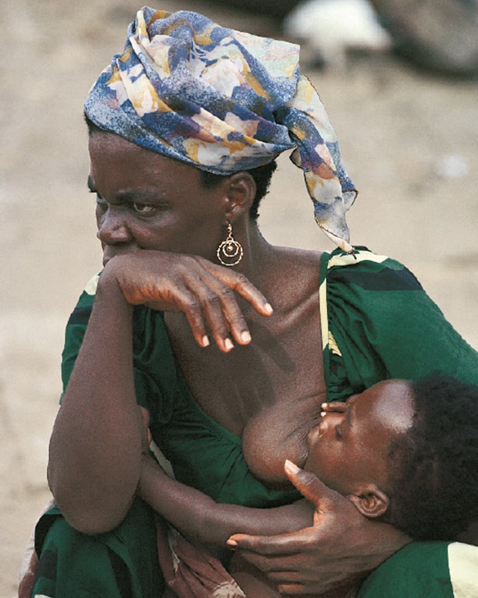 Eine dunkelhäutige Frau mit einem bunten Kopftuch stillt ihr kleines Kind.