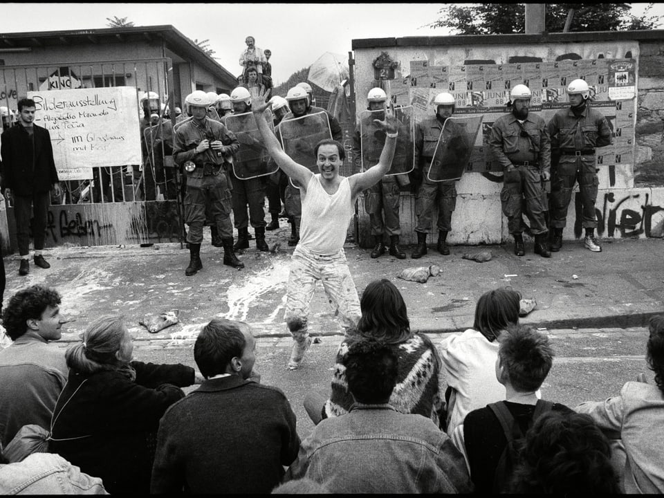 Ein mann tanzt vor einer Gruppe Polizisten in Kampfmontur.