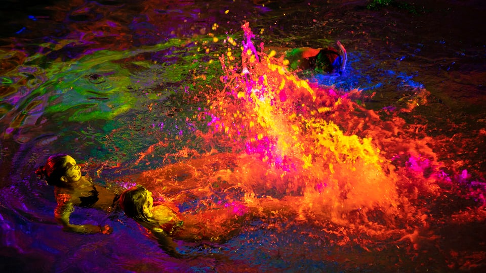 Schwimmende Personen in einem bunt beleuchteten Wasserbecken.