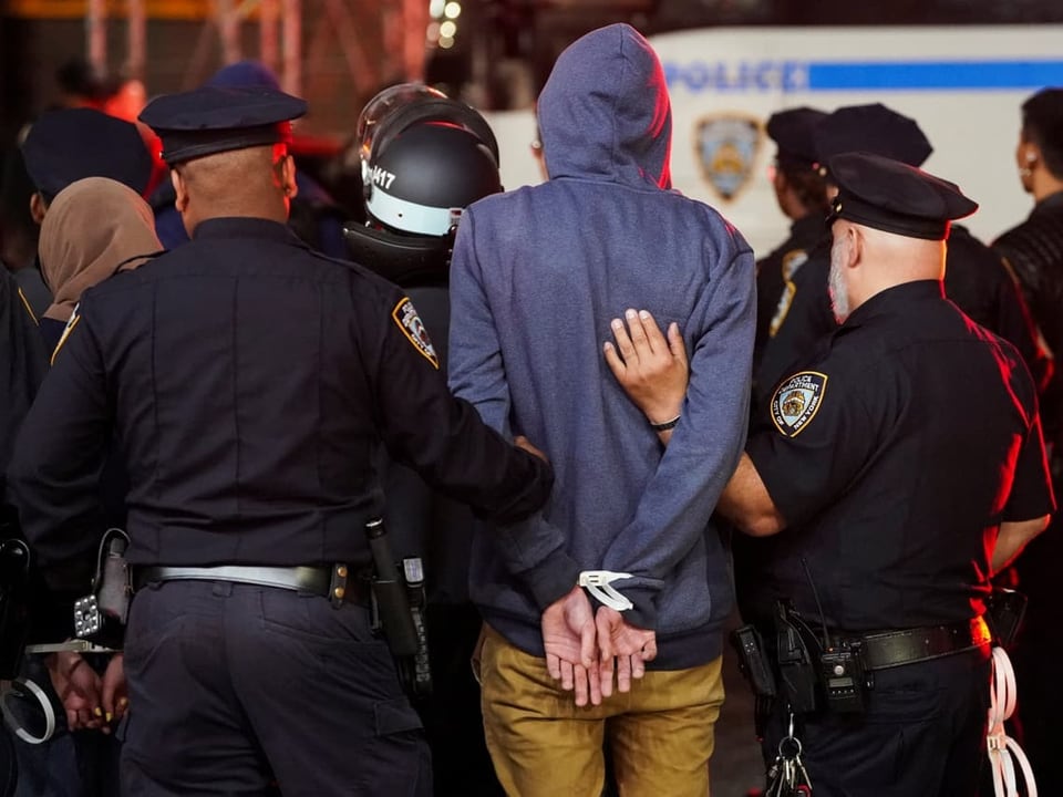 Polizeibeamte führen einen Mann mit Handschellen ab.