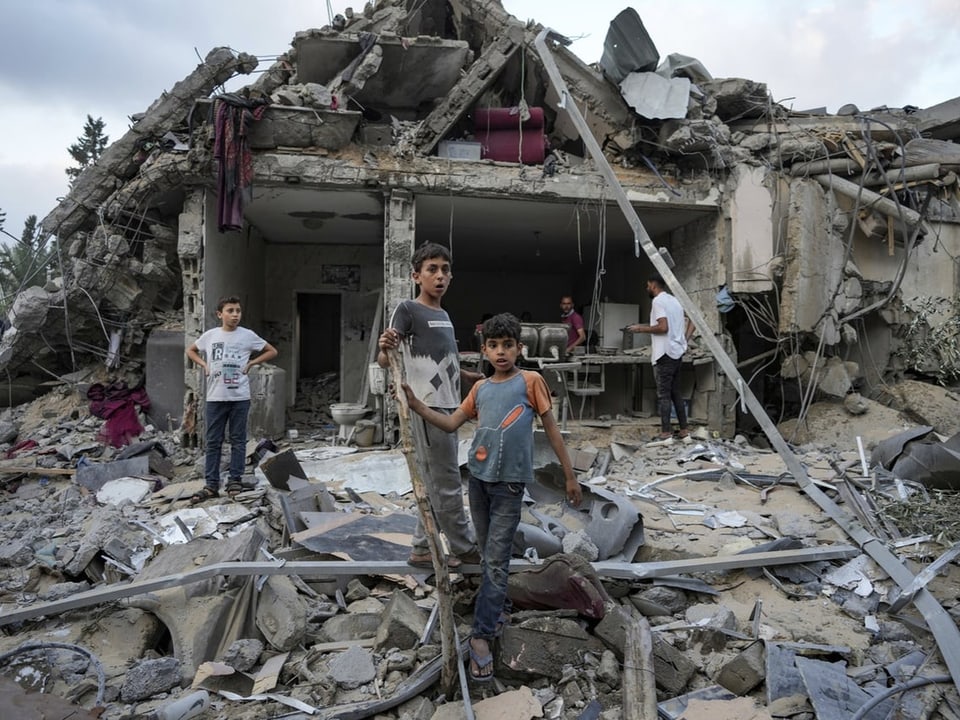Kinder stehen vor einem zerstörten Gebäude mit Trümmern.