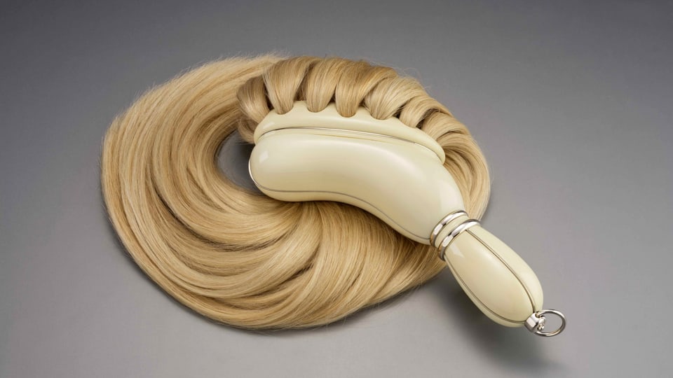 Eine Haarbürste, aus der lange blonde Haare kommen.
