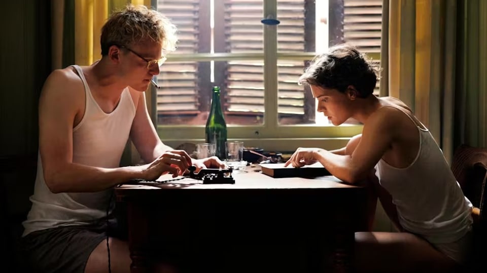 Eine junge Frau und ein junger Mann sitzen in Träger-Shirts am Tisch vor einem Morseapparat.