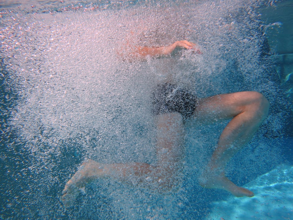 Unterwasserfoto eines beinvoran ins Wasser tauchenden Mannes.