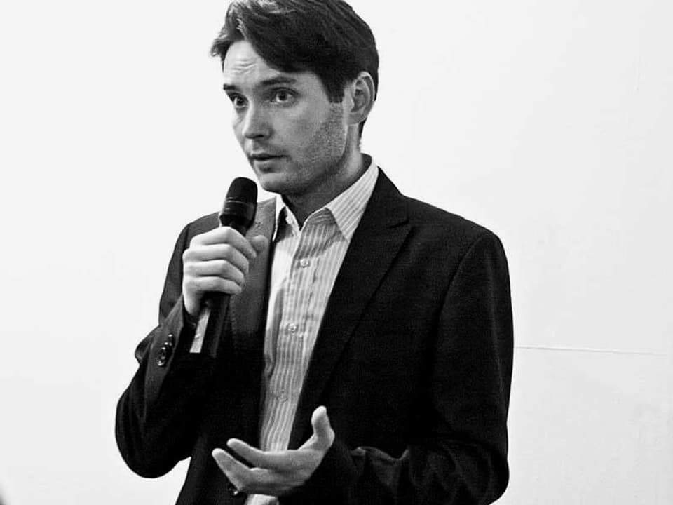 Ein Mann in einem schwarzen Anzug mit einem MIkrofon in der Hand.