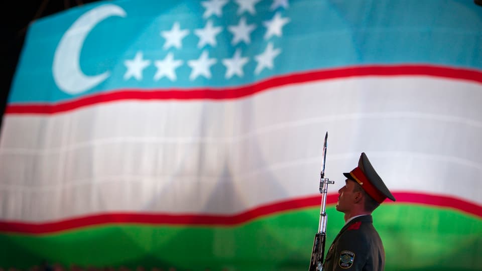 Ein Soldat mit Gewehr vor einer usbekischen Flagge.