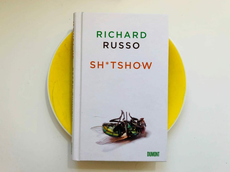 Der Roman «Sh*tshow» von Richard Russo liegt auf einem gelben Teller