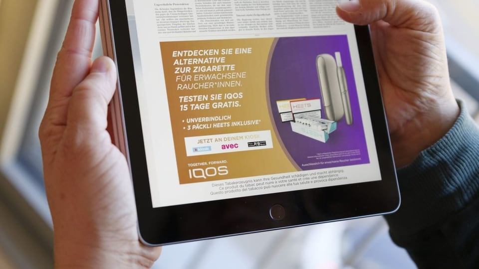 Ein Mann hält ein IPad in der Hand. Auf dem Screen ist Tabakwerbung zu sehen.