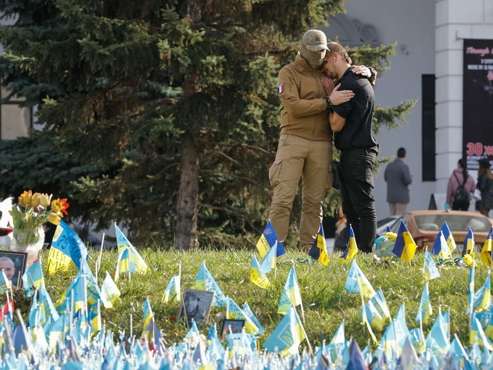 Zwei Männer umarmen sich vor einer Gedenkstätte.