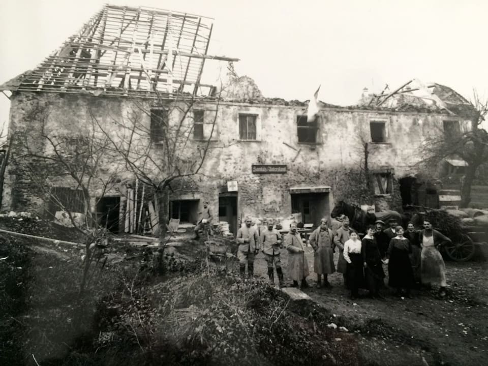 Ein Haus mit zerstörtem Dach, davor stehen Menschen.