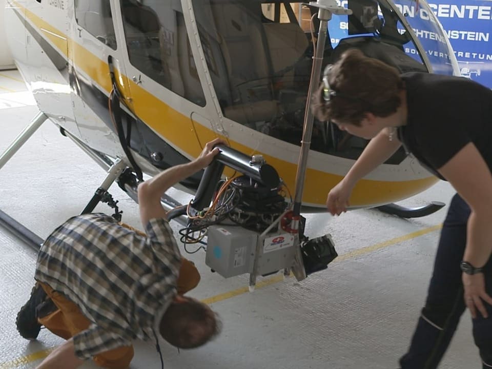 Zwei Menschen untersuchen Gerät am Helikopter
