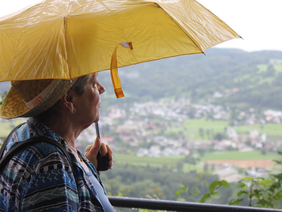Frau mit gelbem Schirm blickt in die Ferne.