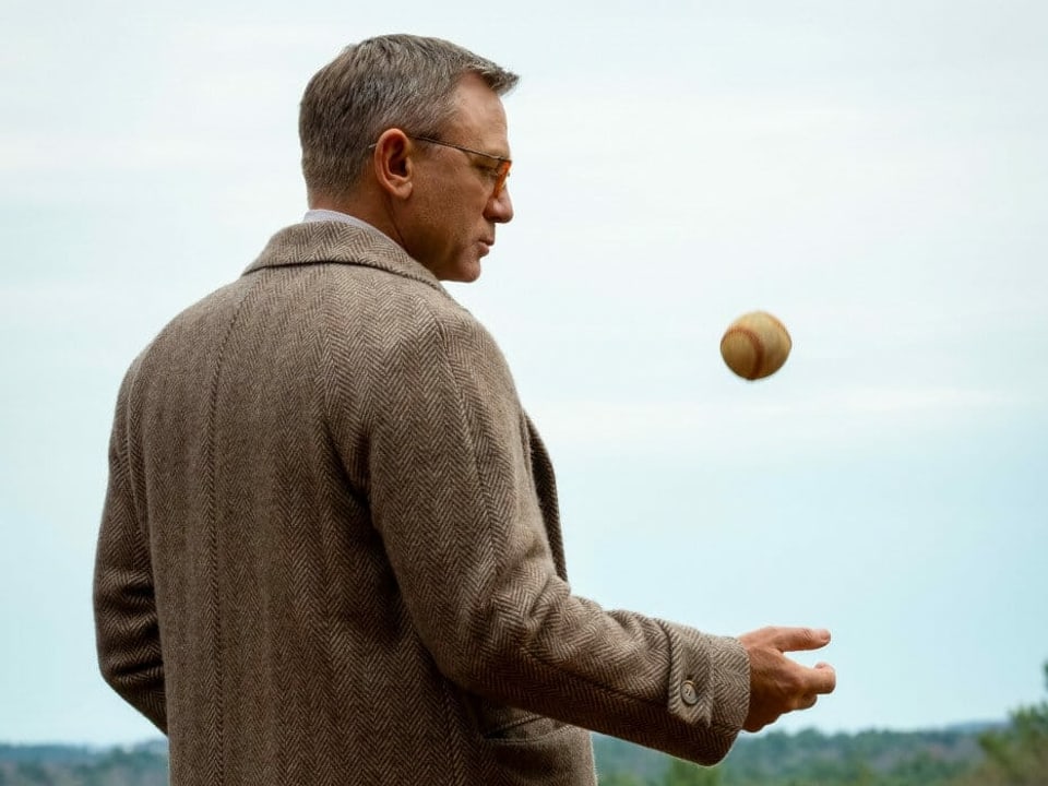 Ein Mann im Mantel spielt mit einem Baseball.