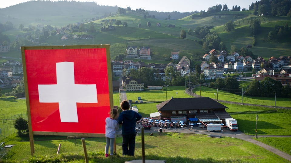 Blick auf Hügellandschaft. Im Vordergrund ist eine Schweizer Fahne zu sehen.