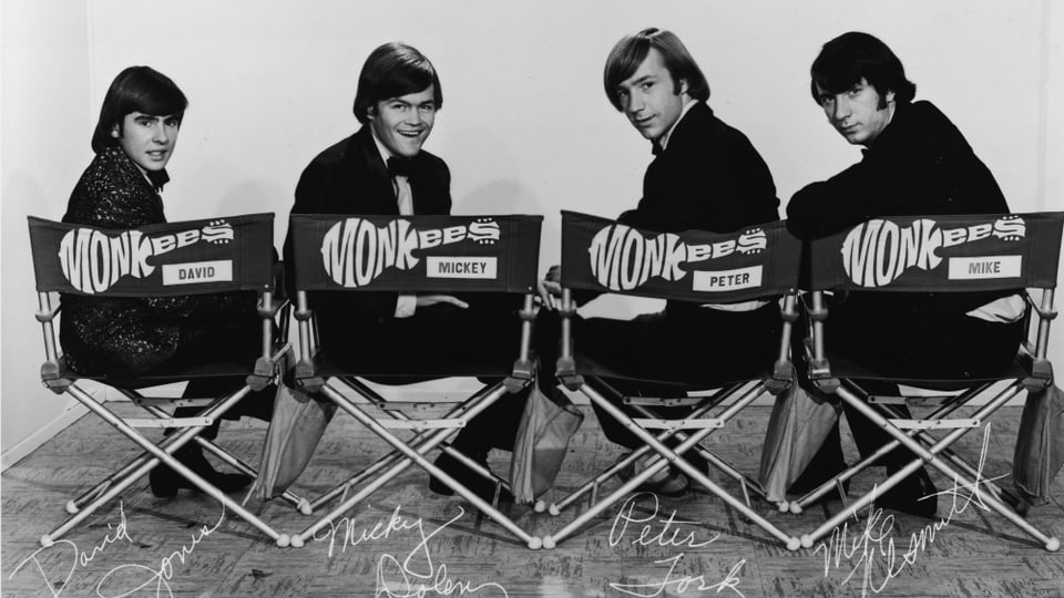 The Monkees sitzen auf Stühlen.