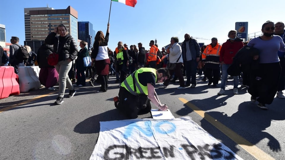 Menschen protestieren am Hafen, einer schreibt ein Plakat mit den Worten «No Green Pass»