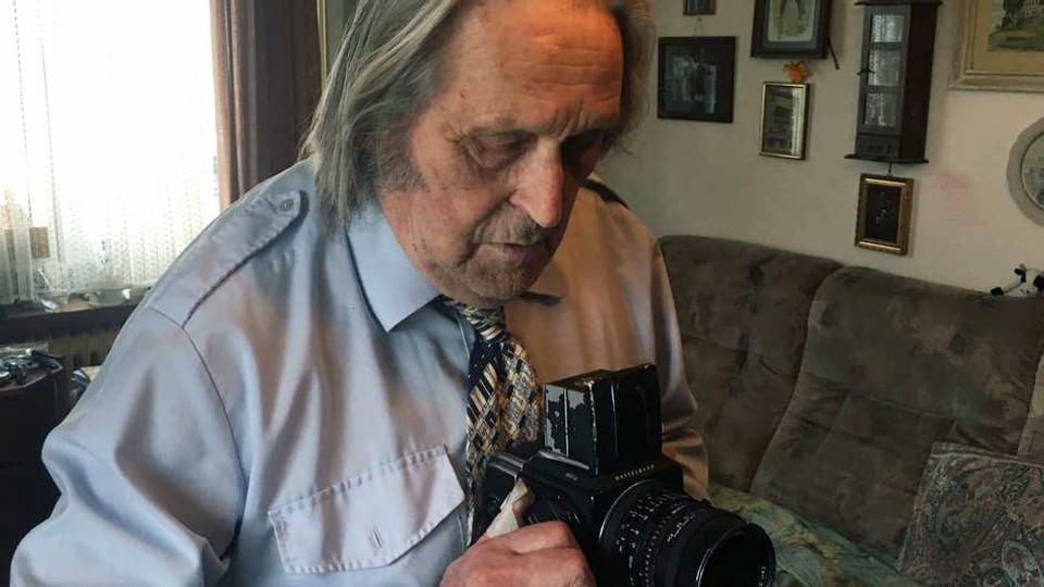 Ein älterer Mann hält eine Kamera.