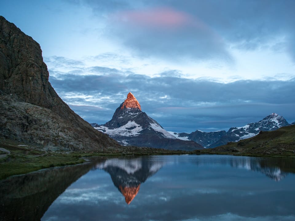 Das Matterhorn wird von der Sonne beschienen und spiegelt sich im Vordergrund im Bergsee.
