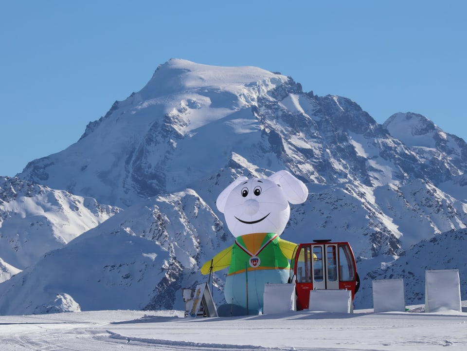 Am Skisammelplatz steht eine rote Gondel und eine mit Luft gefüllte Märchenfigur, es herrschen klare, wolkenlose Bedingungen.
