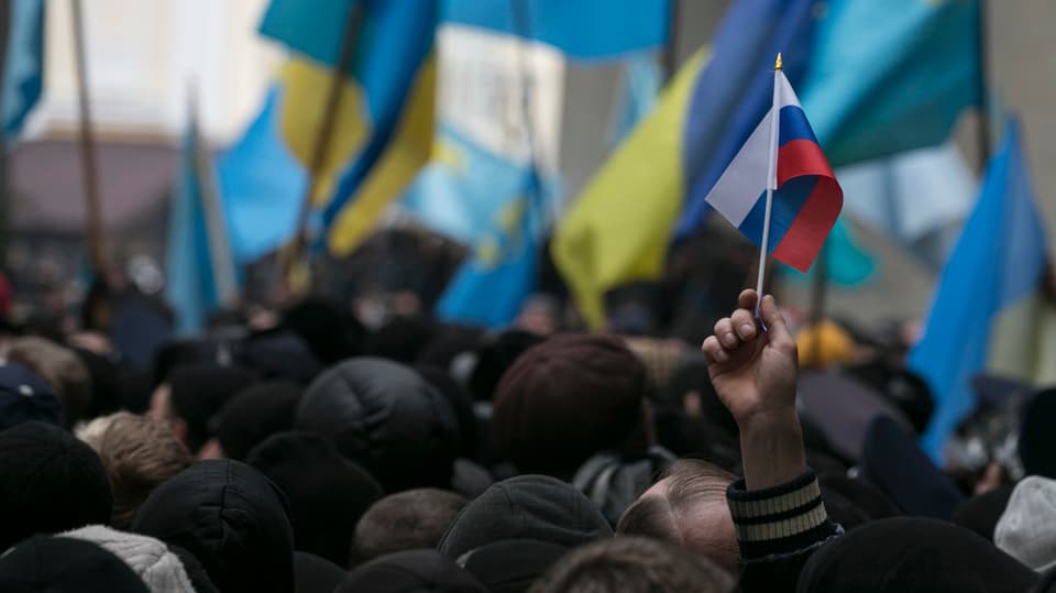 Demonstration in Simferopol vom 26.Februar - viele ukrainische Flaggen im Hintergrund, im Vordergrund streckt ein Demonstrant ein russisches Fähnchen in die Höhe.