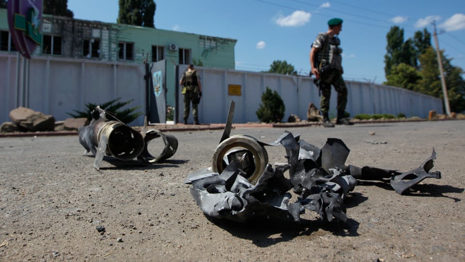 Soldaten stehen vor einem Grenzposten, am Boden liegen Waffen-Bruchstücke