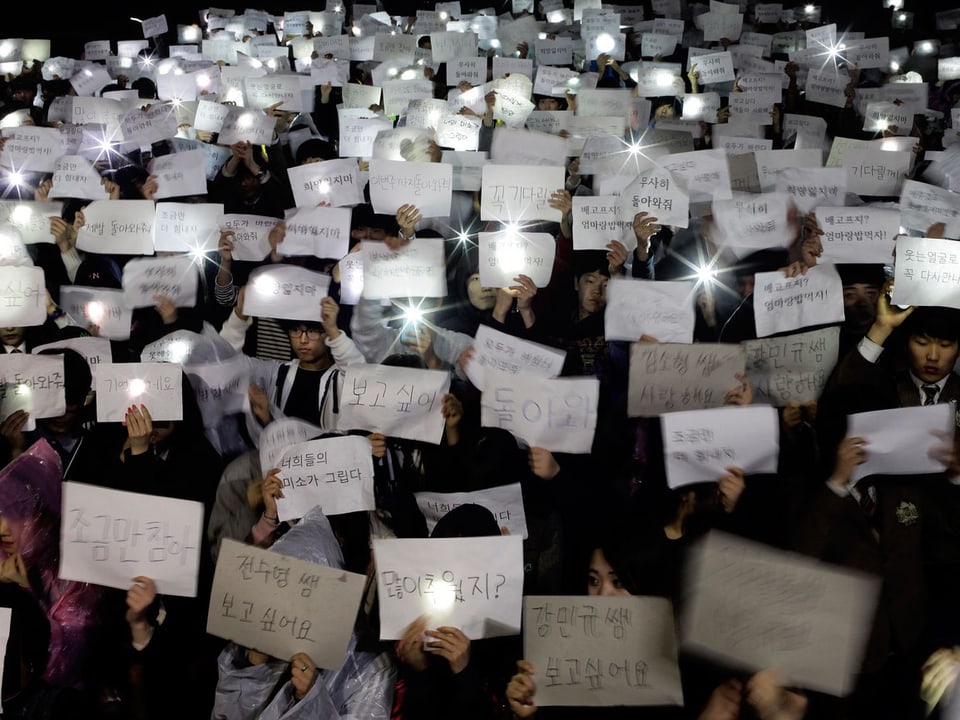 Südkoreanische Studenten halten Botschaften hoch und Kerzen.