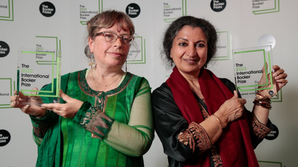 Two women in their mid-fifties in festive attire each hold a trophy for the cameras.