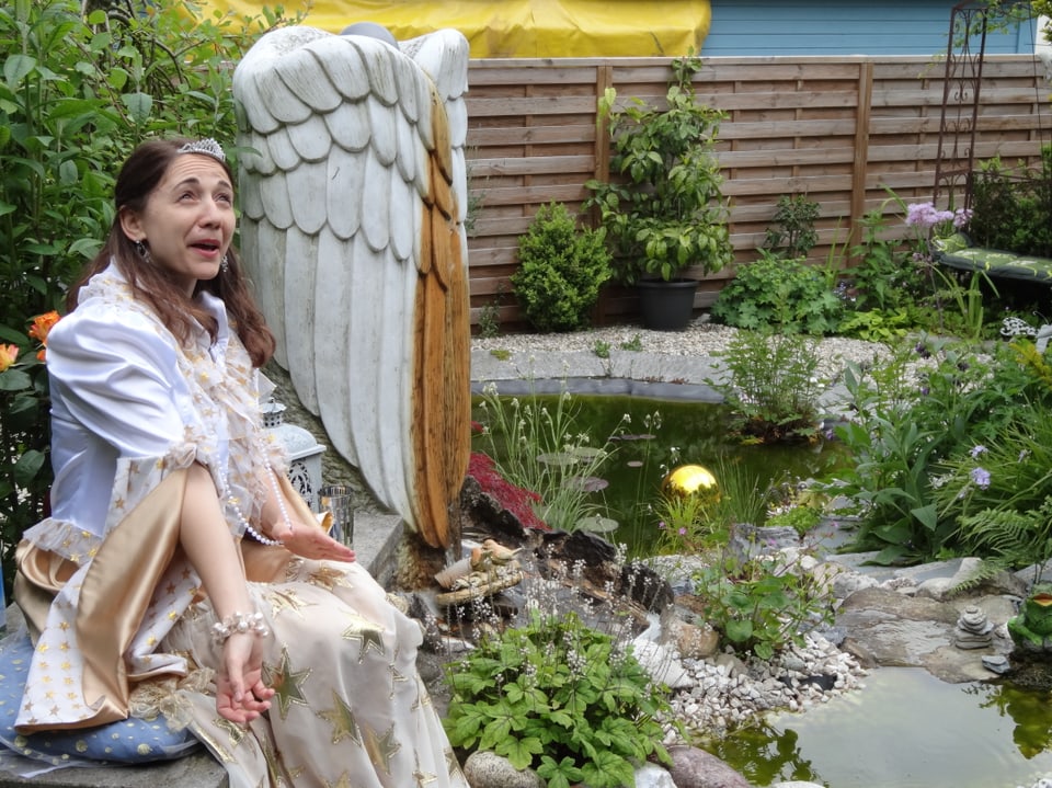 Eine Person sitzt als Märchenfigur verkleidet in einem Garten