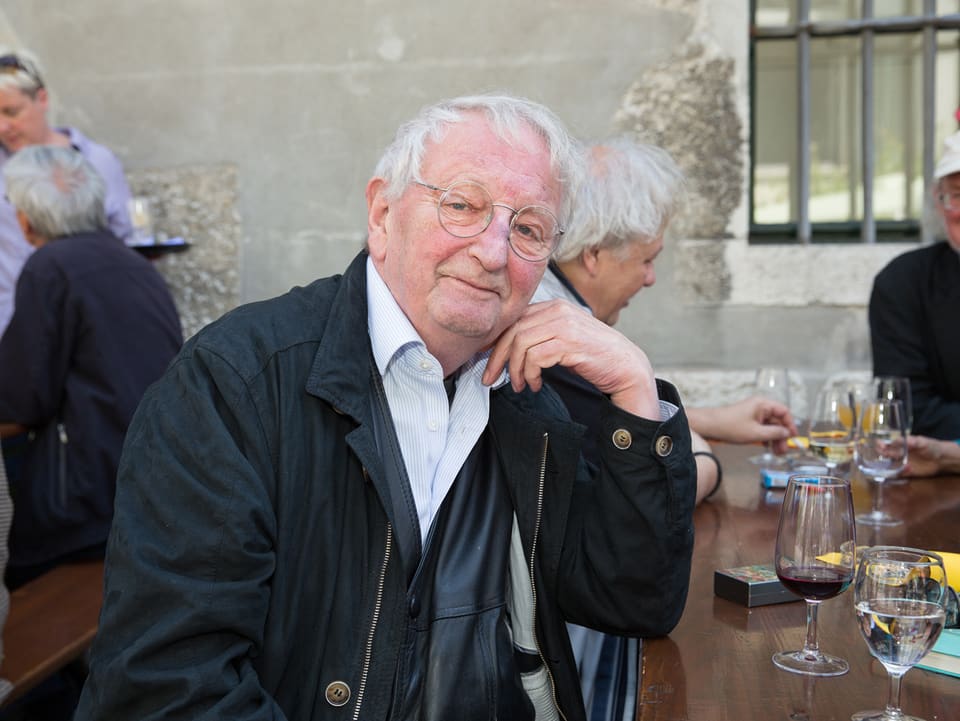 Peter Bichsel sitzt mit einem Glas Wein an einem Tisch.