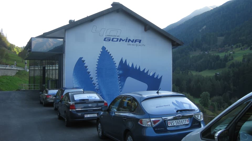 Ein Gebäude an einem Talhang, daneben stehen Autos.