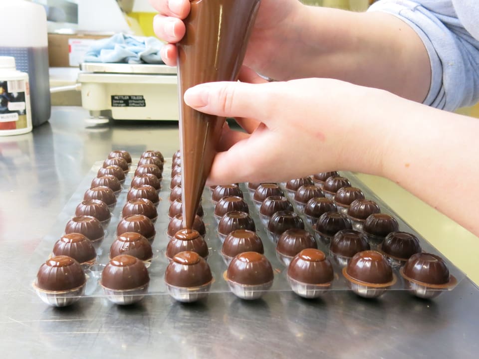 Pralinen werden mit einem Spritzsack mit Schokolade gefüllt. 