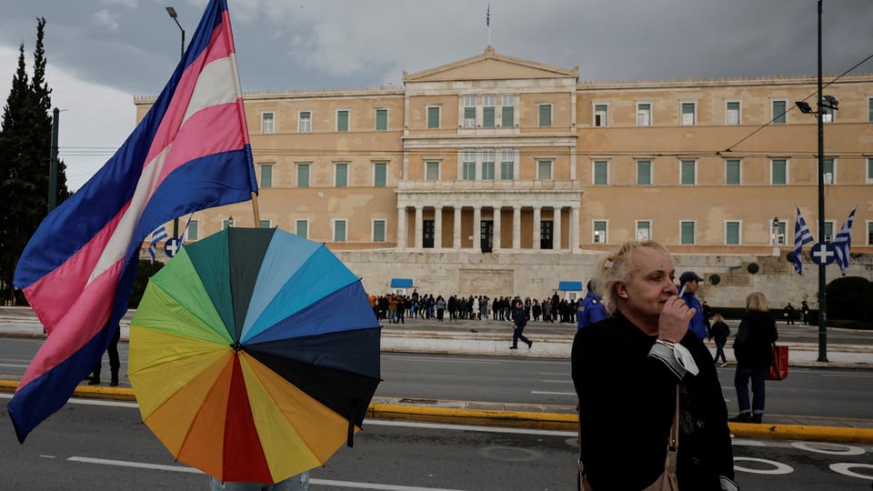 Das Parlamentsgebäude, im Vordergrund steht eine Person mit einem Regenbogen-Schirm.