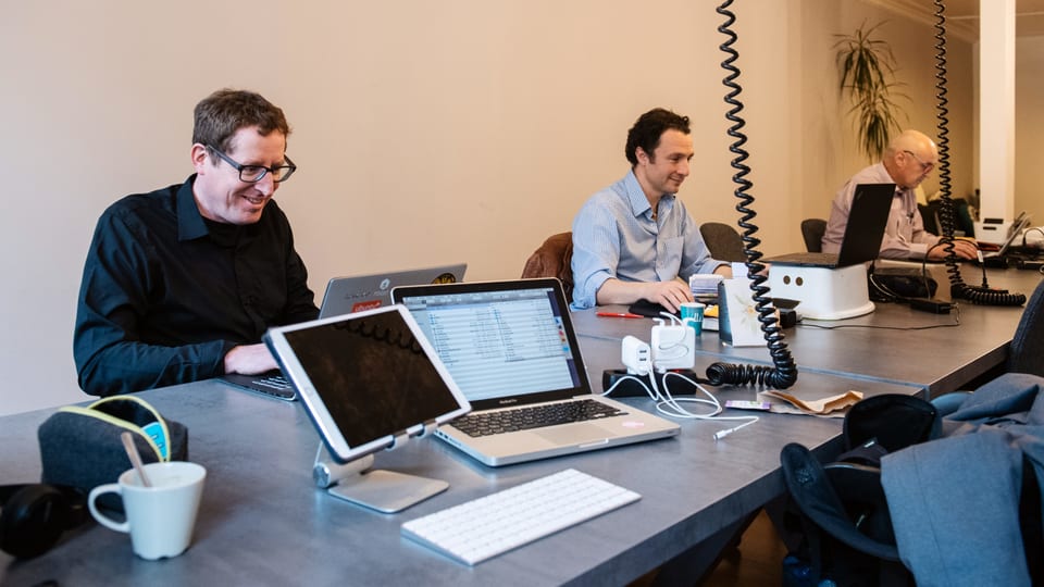 Drei Männer sitzen an einem langen Tisch vor ihren Laptops.