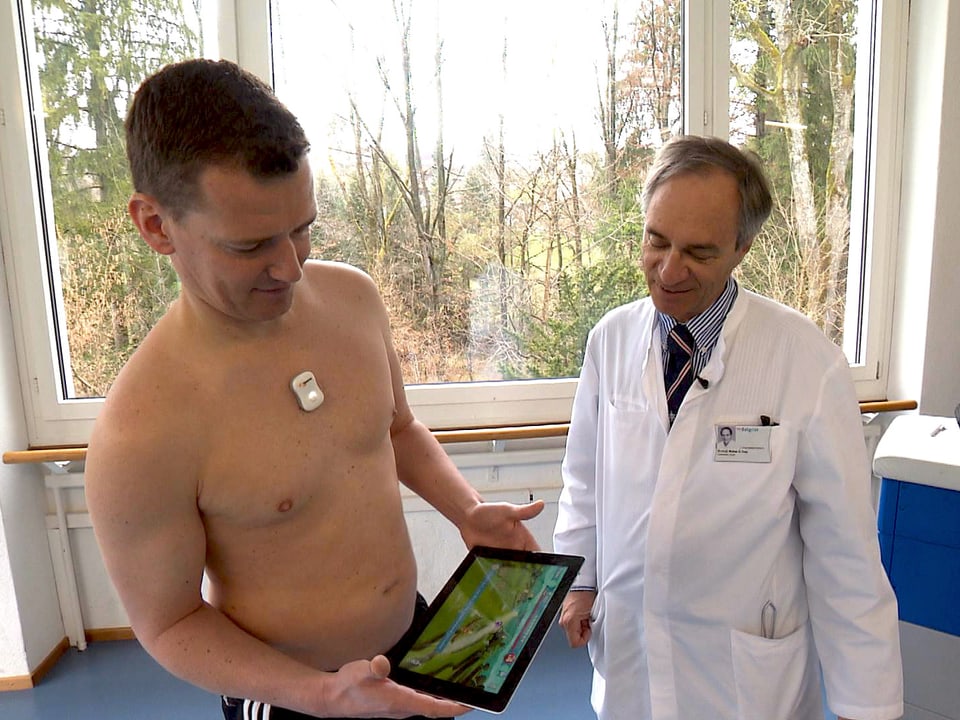 Mann mit nacktem Oberkörper hält ein Tablet, daneben ein Arzt im weissen Kittel.