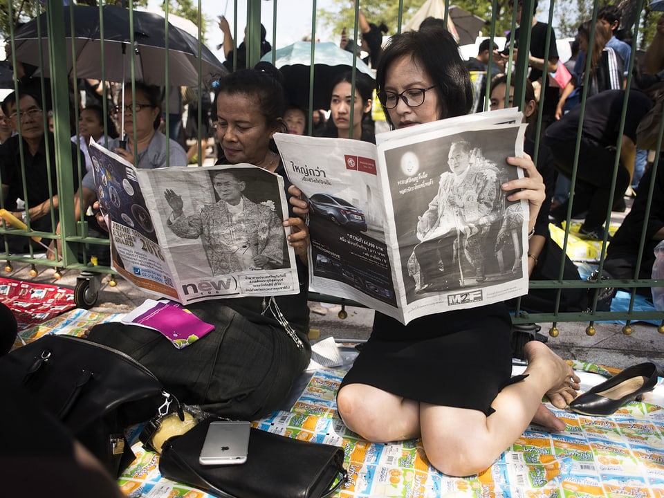 Zwei Frauen sitzen am Boden und lesen in einer Zeitung über den Tod von König Bhumibol. (getty images)